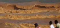 Homens observam uma onda de lama se quebrar na praia em Regência (Foto: Ricardo Moraes/Reuters)